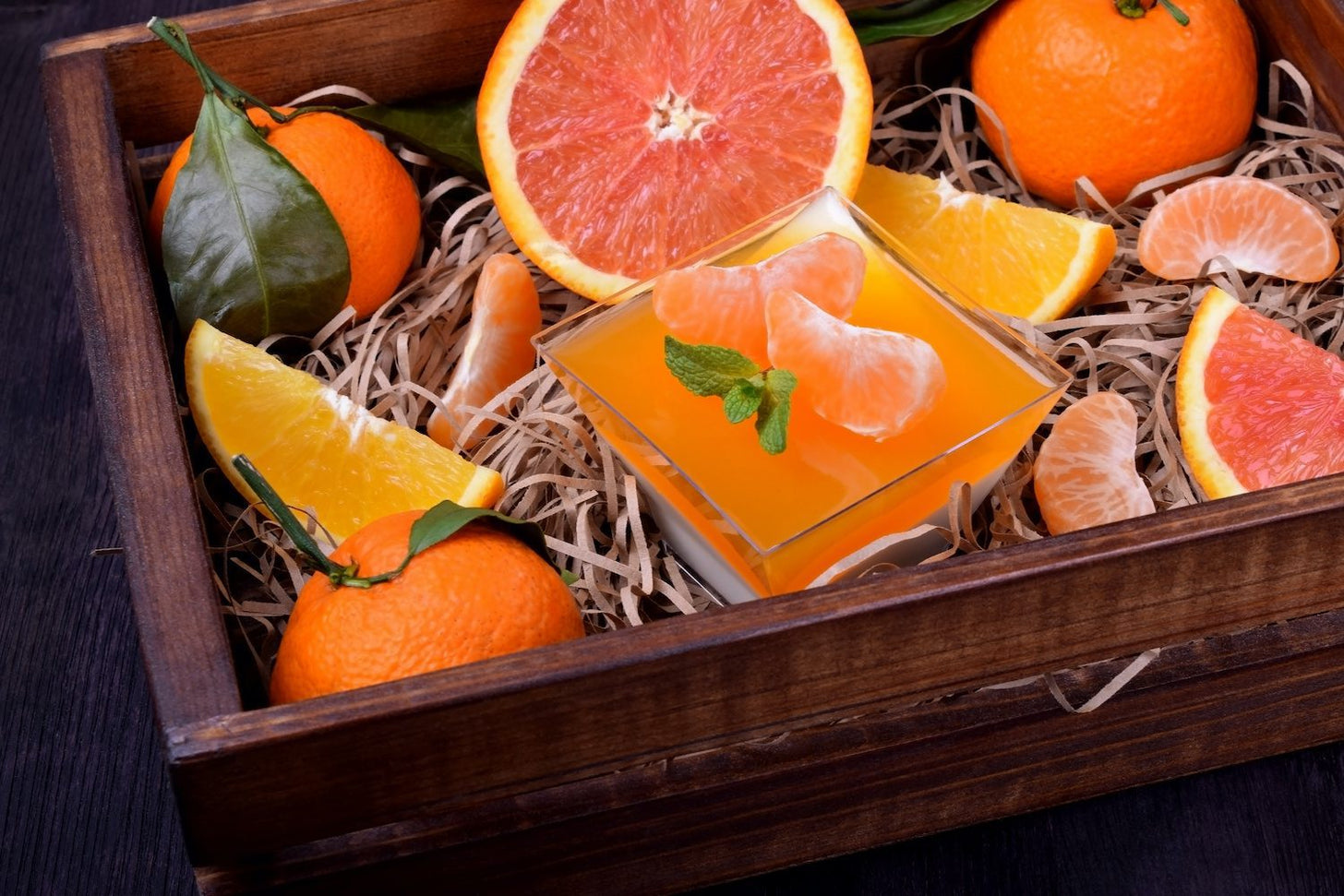 A box with citrus fruits and a bowl of orange gelatin inside