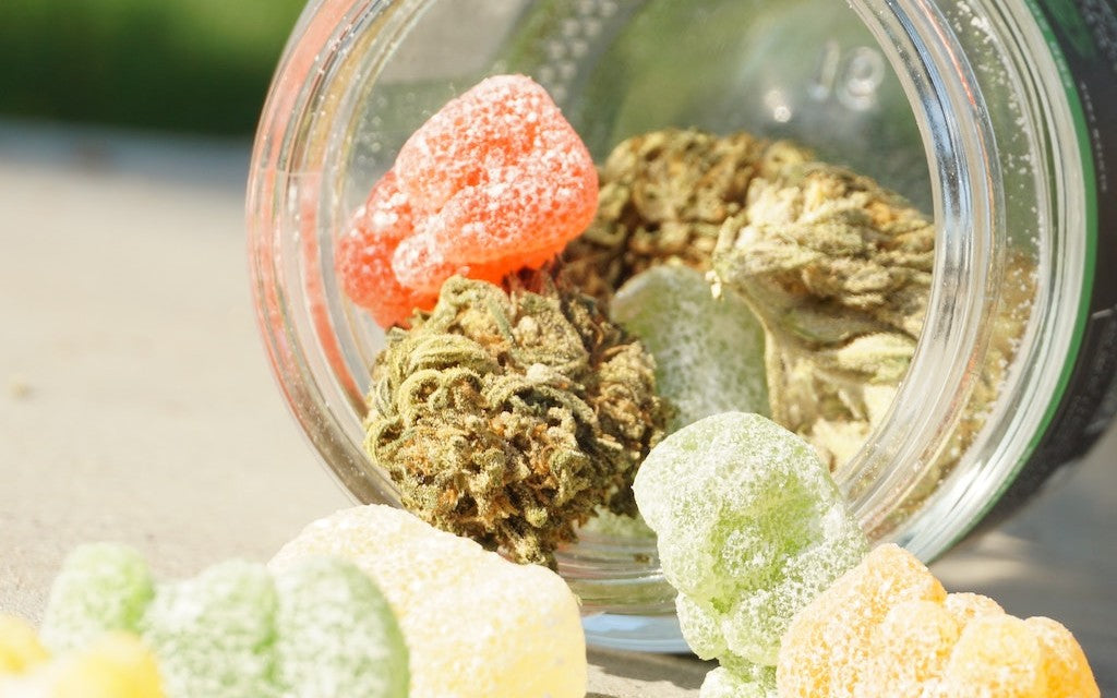 Hemp buds and CBD gummies tumbling out of an open jar