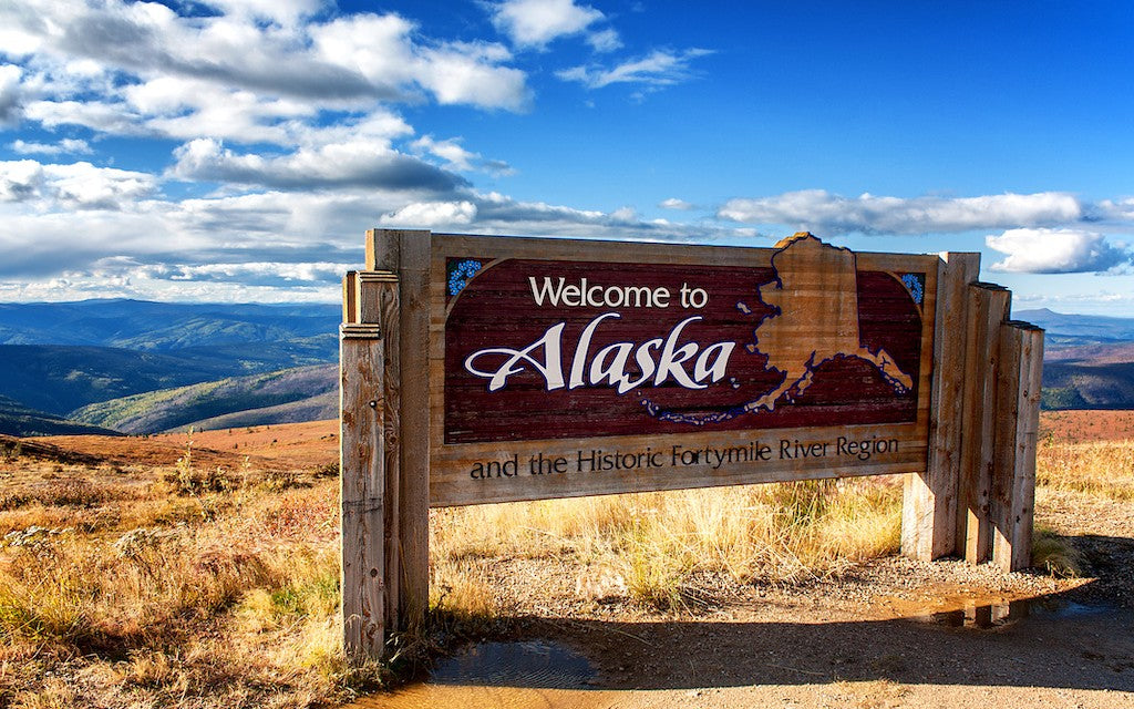 A welcome to Alaska sign in a prairie setting under a blue sky