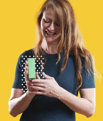 Woman smiling and holding a small green FAB CBD oil box against a bright yellow background