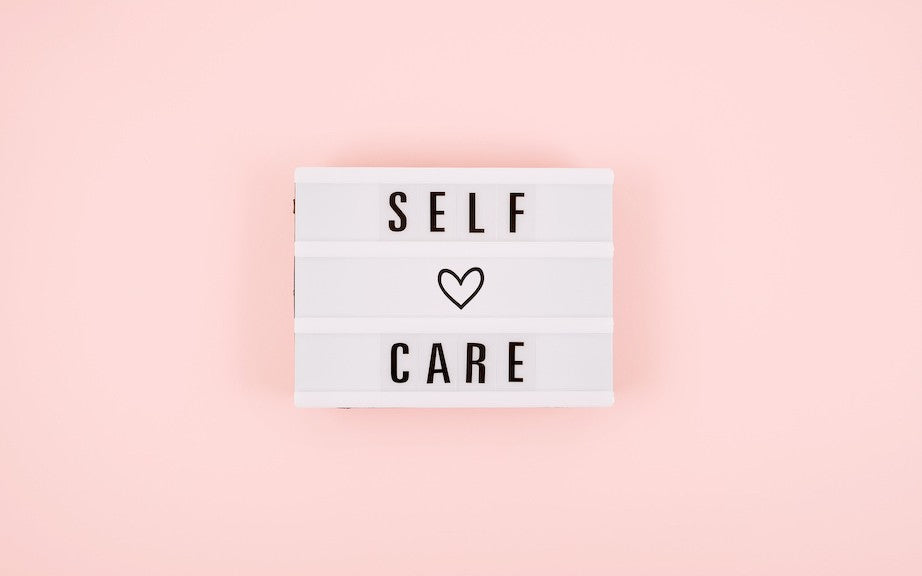 A simple black and white sign that says "SELF CARE" with a heart, placed on a pink background