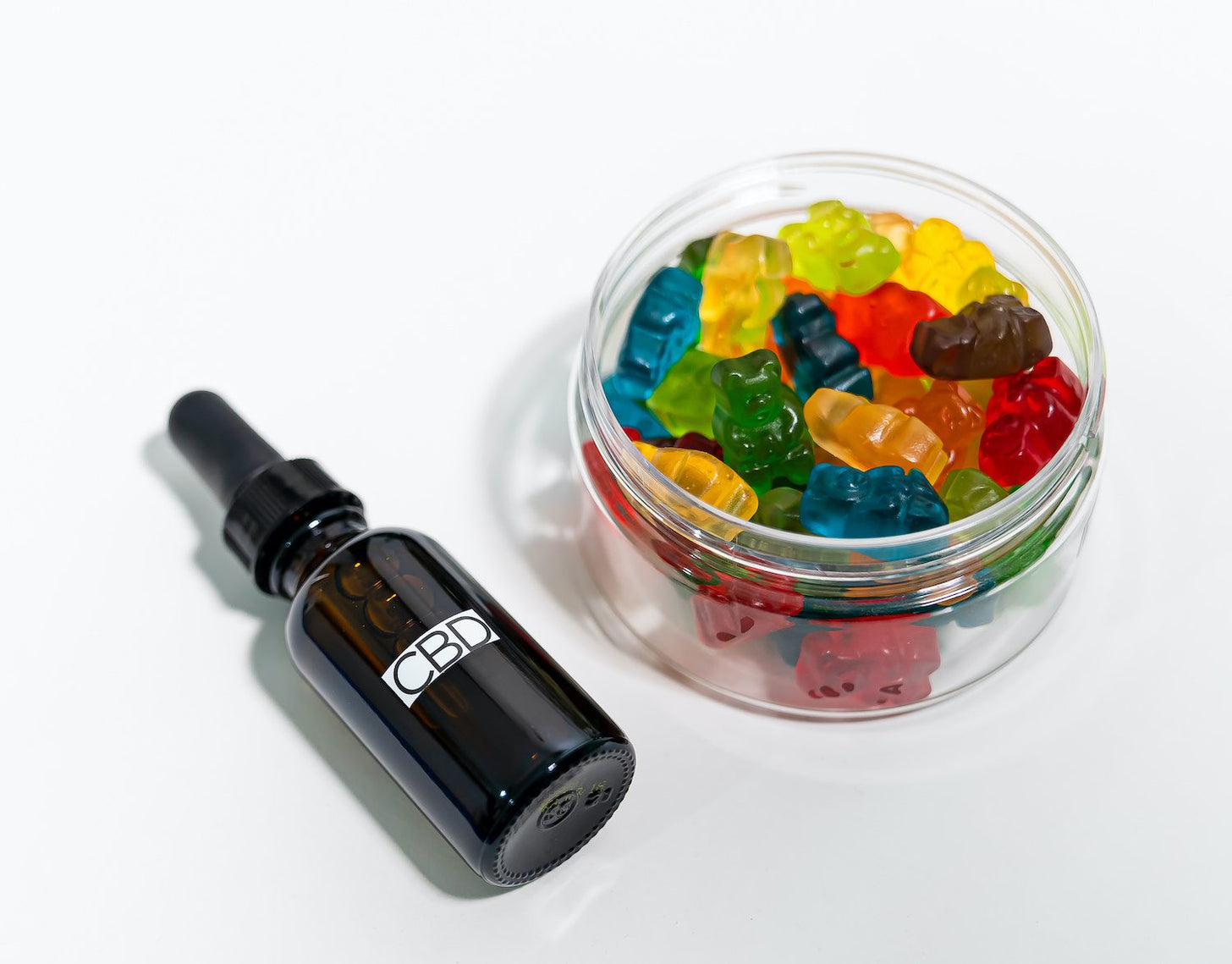 A bowl of gummies next to a bottle of CBD