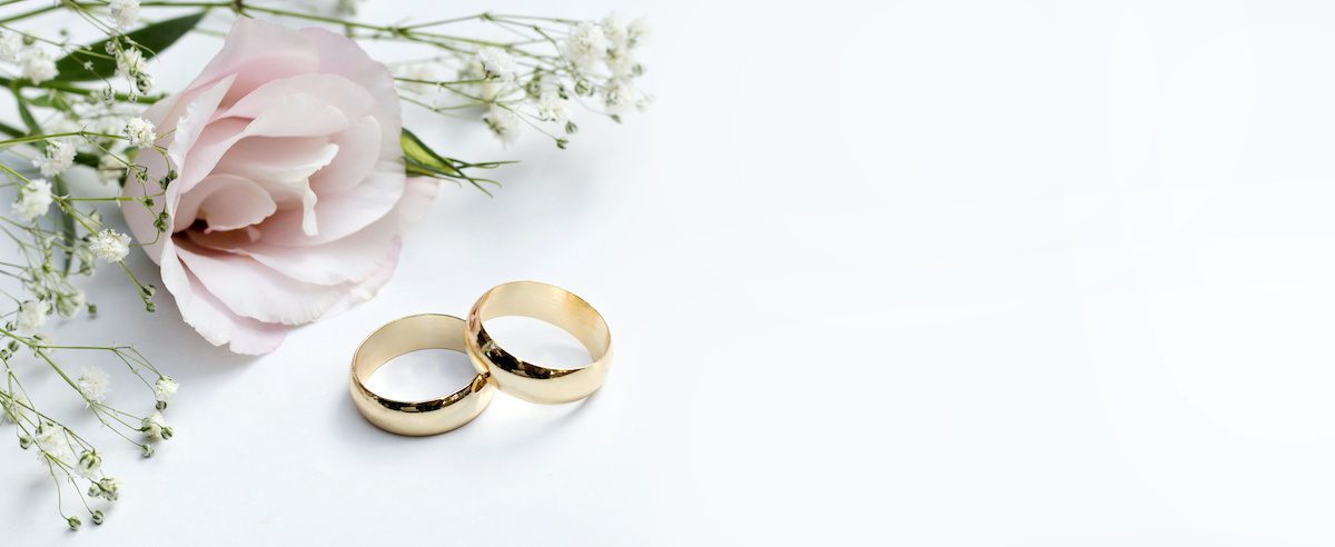 two golden wedding rings next to a dusty pink corsage on a white surface