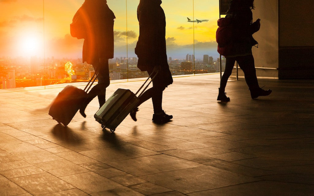Travelers walk through an airport with the sun setting in the window behind them