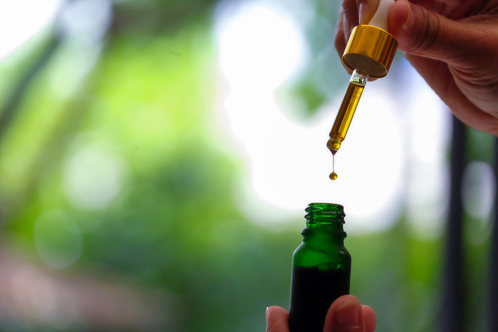 A dropper of CBD oil is squeezed into a dark green glass bottle