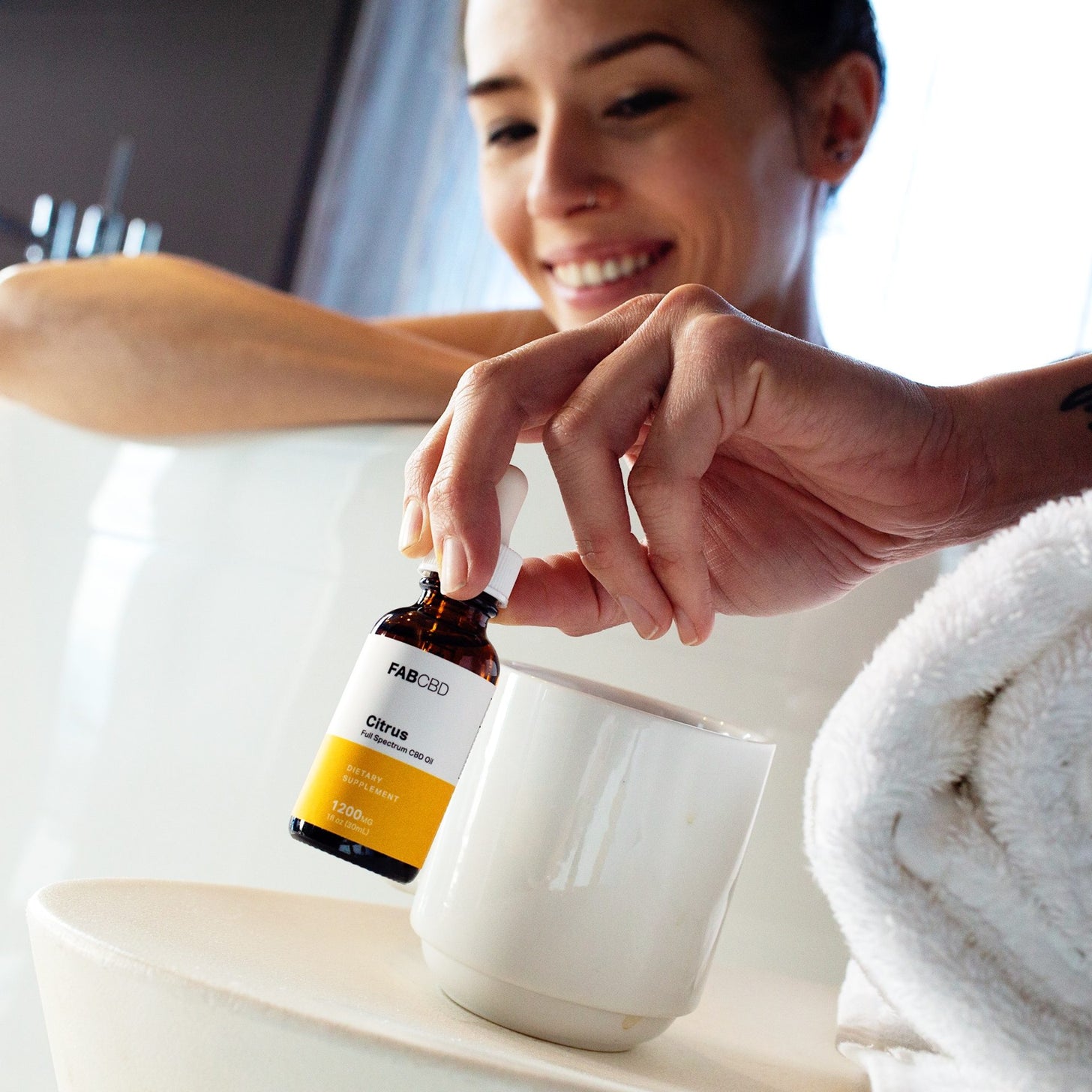 A woman reaches out of the bathtub for a bottle of CBD oil