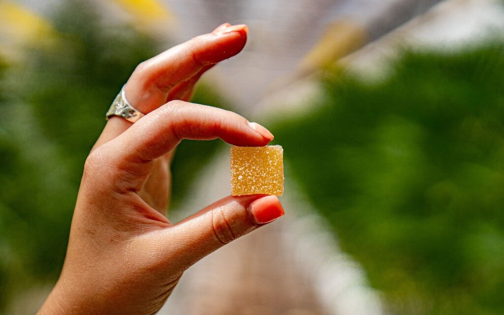 A young woman's hand holds up a square, yellow gummy