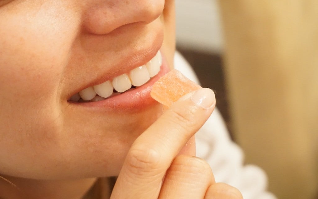 A woman holds a CBD gummy up to her lips