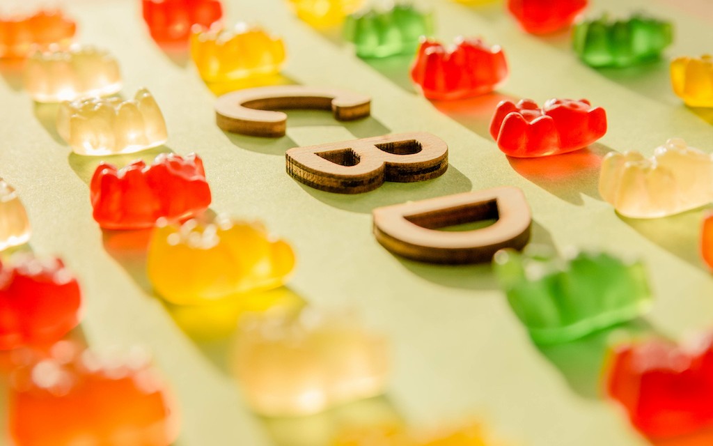 Rows of colorful gummy bears laid out on a surface with the word "CBD" in the middle