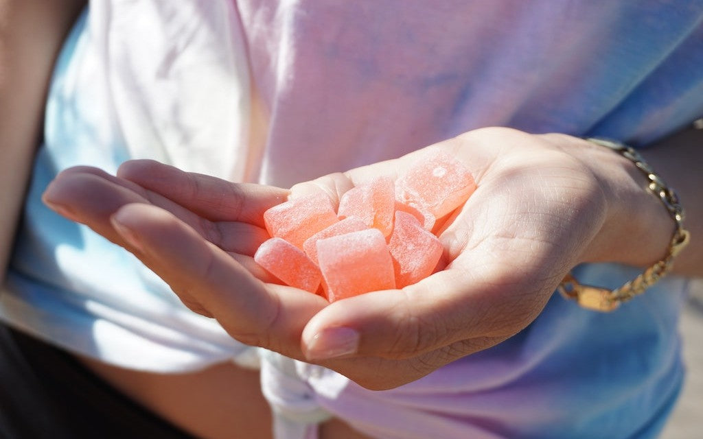 A woman standing in the sun holds a handful of pink CBD gummies
