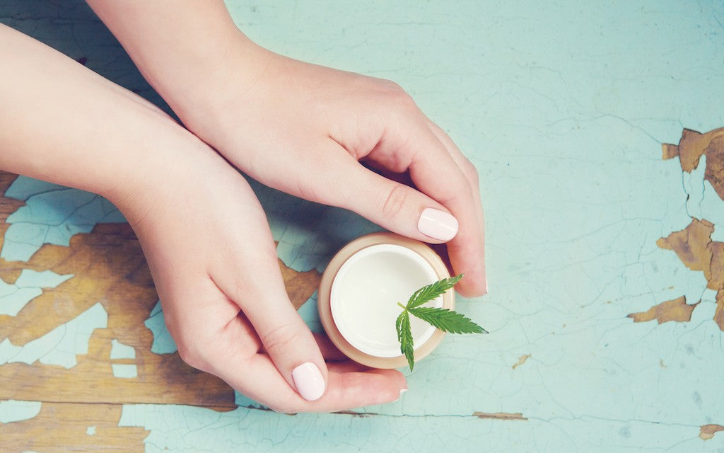 A woman's hands cup a container of cream with a green leaf on top of it