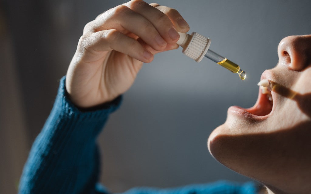 Profile of a woman in a blue sweater dropping CBD oil under her tongue