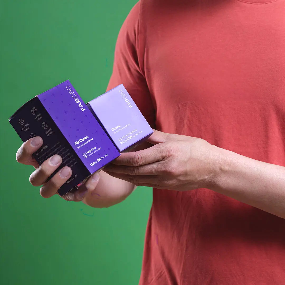 Person holding purple and lavender Anytime + Sleep Gummy Bundle boxes against green background.