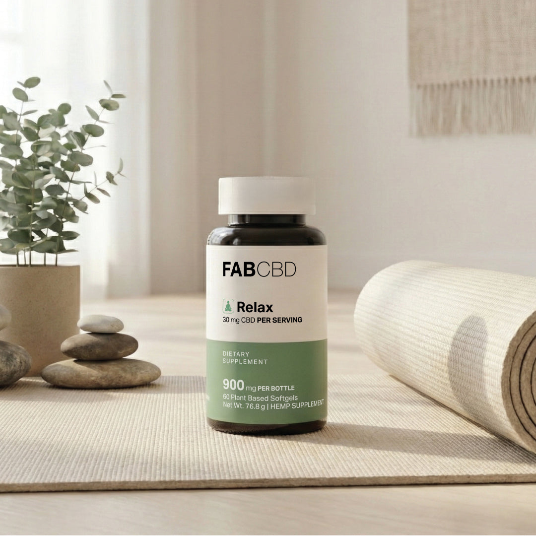 Centered front view of a FABCBD CBD Softgels bottle on a neutral yoga mat with stacked stones, a potted plant, and soft natural light.