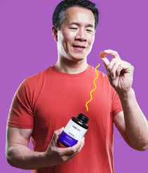 Man in red shirt holding an open FABCBD bottle and lifting an orange gummy toward his mouth against a purple background