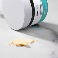 White jar of FABCBD topical concentrate cream with teal label and cream spread on marble surface.
