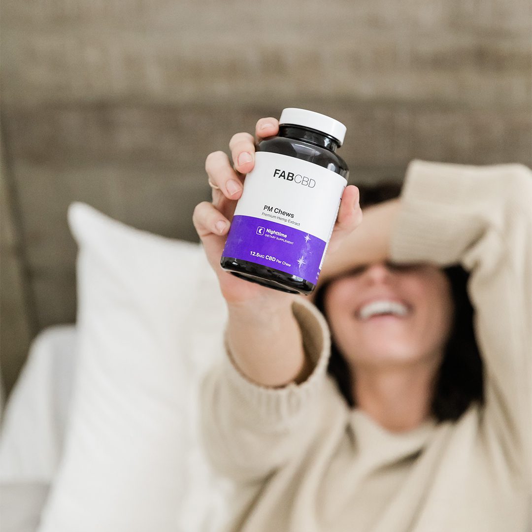 Hand holding a bottle of Fab CBD Sleep Gummies with a white label and purple accent, blurred background.