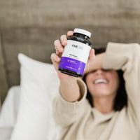 Hand holding a bottle of Fab CBD Sleep Gummies with a white label and purple accent, blurred background.