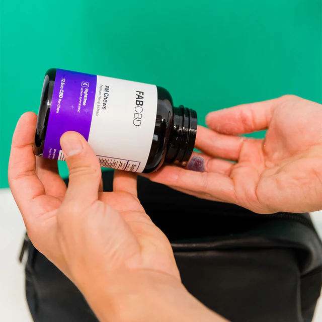 Person pouring purple-labeled FAB CBD gummies from black bottle into hand over black pouch.