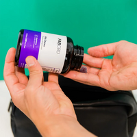 Person pouring purple-labeled FAB CBD gummies from black bottle into hand over black pouch.