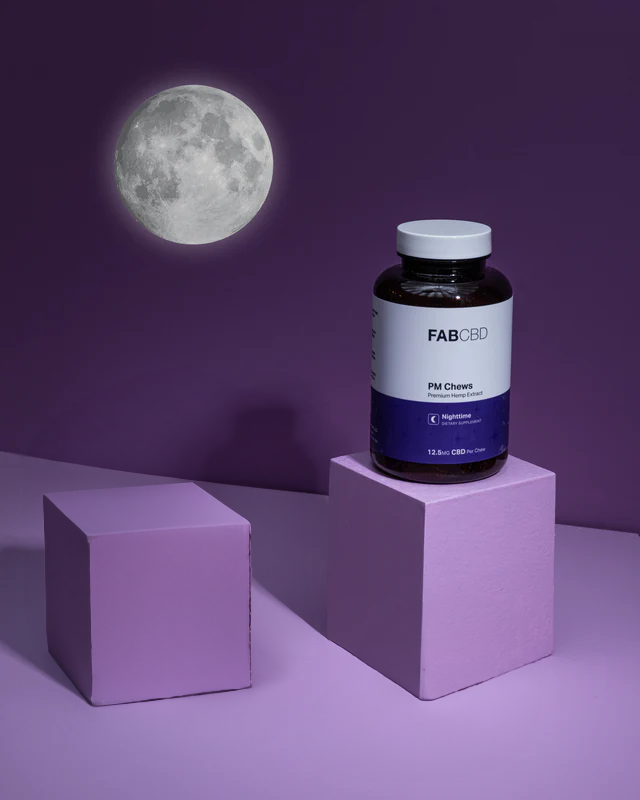 Dark blue bottle of Fab CBD Pill Chews on a lavender cube with a full moon backdrop on deep purple background.