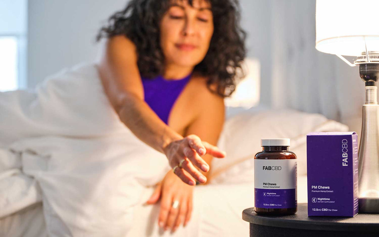 woman in bed reaching for bottle of cbd gummies