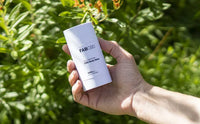 Hand holding a white 2.5oz Salve - 3 Pack stick labeled "FABCBD" against a sunlit green foliage background.