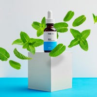 Centered front view of the CBD Oil bottle with mint leaves floating around it on a pale blue background