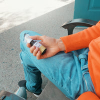 Close-up of a seated person holding a small amber dropper bottle of CBD Oil in their right hand against ripped blue jeans and an orange sweater.
