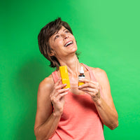 Three-quarter view of a smiling woman holding a yellow box and dropper bottle of CBD Oil against a bright green background