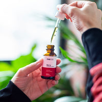 Close-up of a hand holding a FAB CBD CBD Oil dropper bottle as another hand lifts a filled pipette over the amber opening.