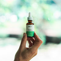 Handheld bottle of CBD Oil held between thumb and forefinger against a soft green bokeh background.