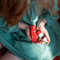 Top-down view of a person in a teal dress holding a red box and bottle of CBD Oil in soft natural light.
