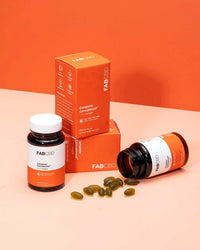 A product display for FAB CBD Complete Cannabinoid™ 1:1:1:1 Softgels on an orange background. Two orange packaging boxes are stacked behind an upright bottle and a bottle tipped on its side with dark green softgels spilled out. The packaging displays key specifications: a CBC+CBG+CBD+CBN hemp supplement formula, 15MG per serving, and 60 plant-based softgels.