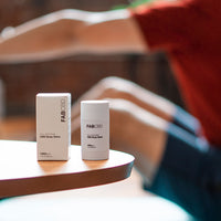 Close-up of FABCBD CBD Body Salve and its box on a rounded wooden table edge with a blurred person stretching in the background.