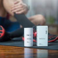 Close-up of FABCBD CBD Body Salve packaging and stick on a workout mat with blurred athletic legs and shoes in the background.