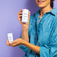 Woman in a blue shirt holding a white stick applicator of FAB CBD CBD Body Salve upright near her face against a lavender background